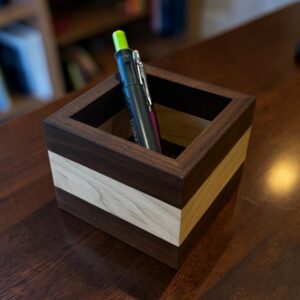A walnut and maple square desk tidy showing pens on a wooden desk.