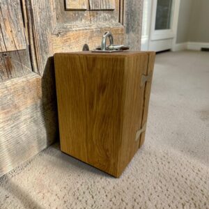 Solid oak doorstop with brass inlays holding together a large split and a chrome lifting handle on top all holding open a rustic door.