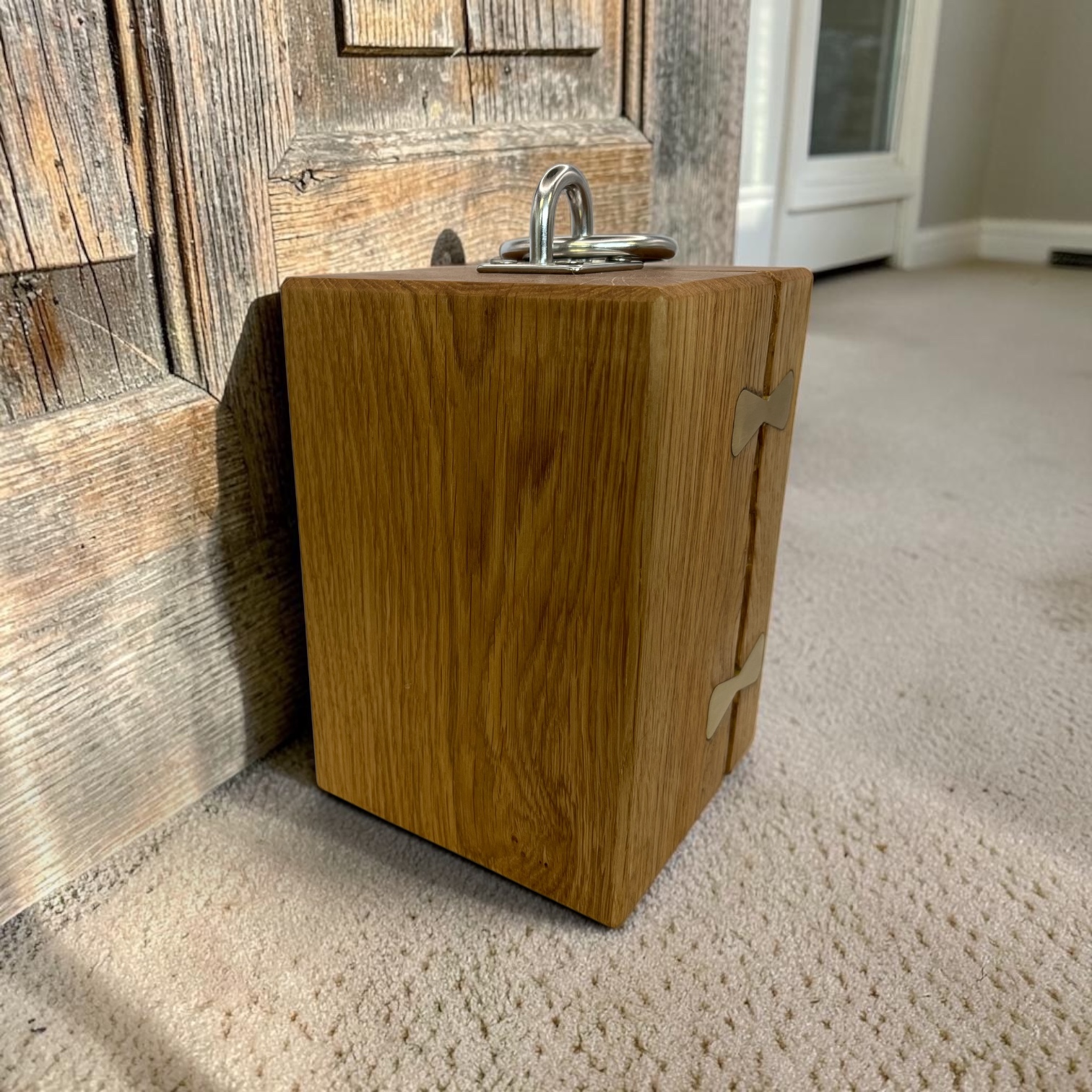 Solid oak doorstop with brass inlays holding together a large split and a chrome lifting handle on top all holding open a rustic door.