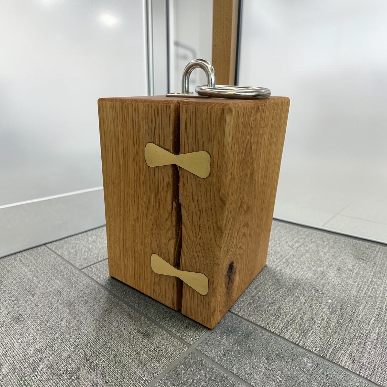Solid oak doorstop with brass inlays holding together a large split and a chrome lifting handle on top.