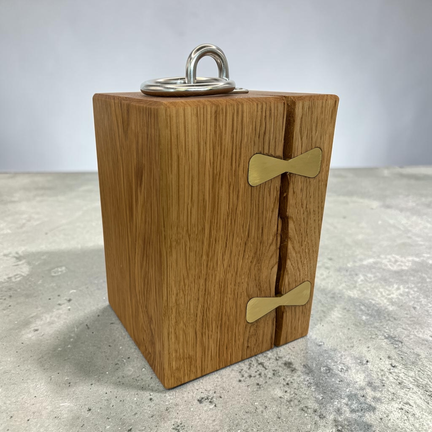 Solid oak doorstop with brass inlays holding together a large split and a chrome lifting handle on top.