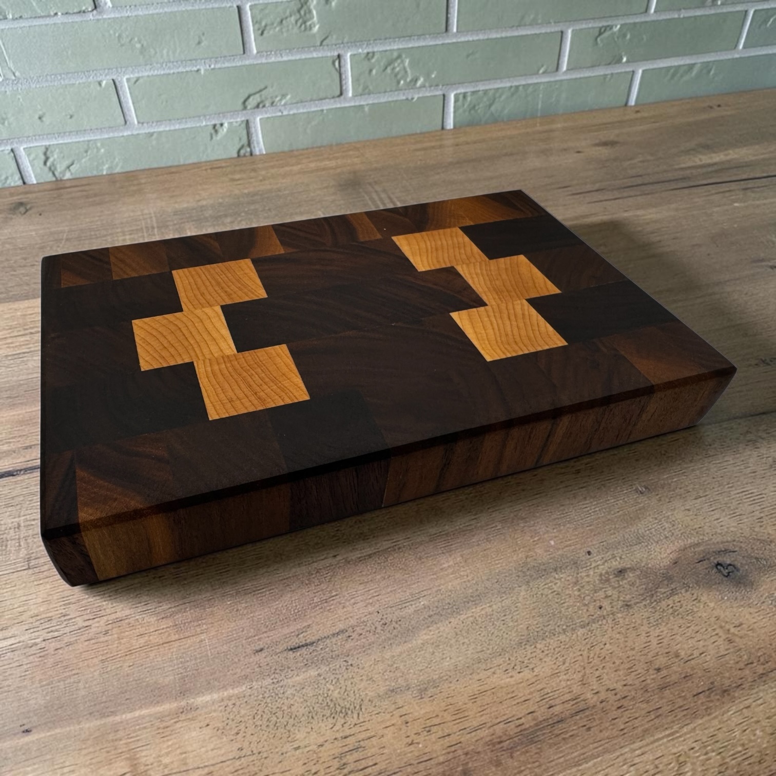 End grain chopping board made of walnut and maple on a oak worktop with sage tiles behind.