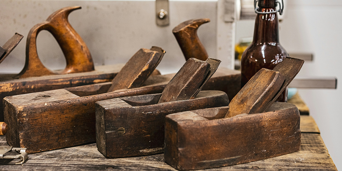 A series of old hand planes on a workbench with a bottle of beer behind