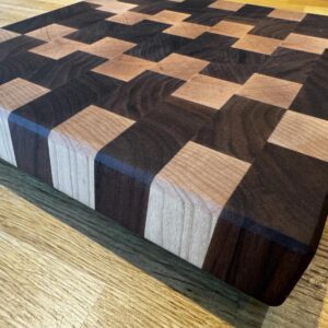 End grain chopping board made of walnut and maple on a rustic worktop.