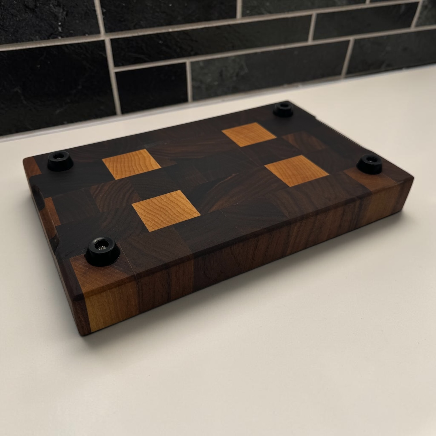 End grain chopping board made of walnut and maple on a white worktop showing the feet and handles.