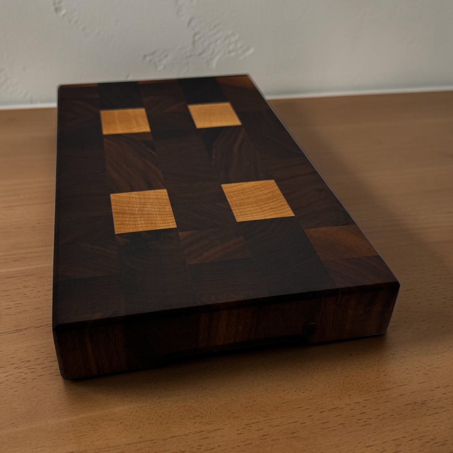 End grain chopping board made of walnut and maple on a rustic worktop.