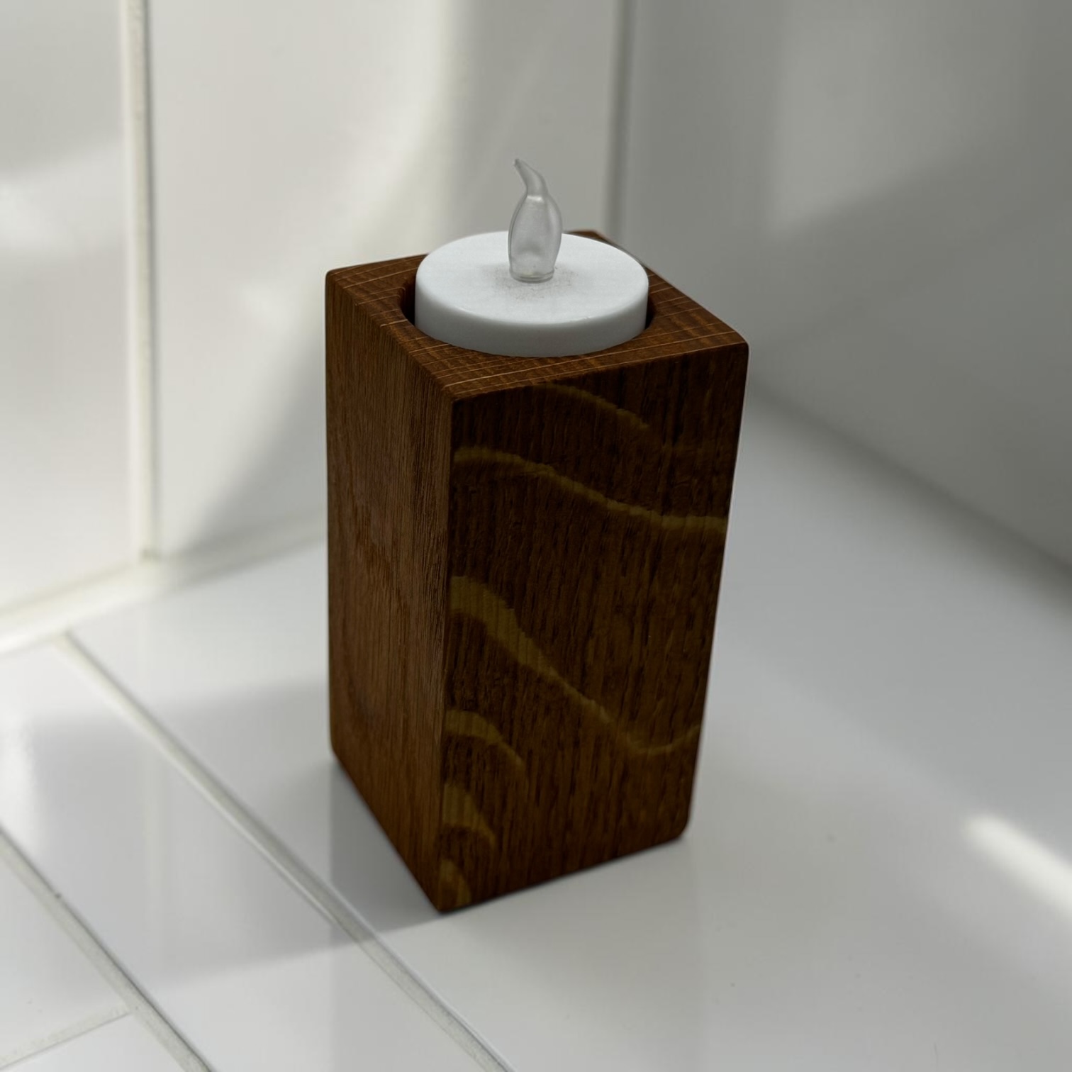 A medium tea light holder that is tall and square with an electric tea light in the top.