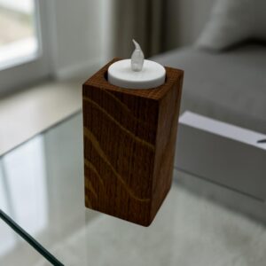 A medium tea light holder that is tall and square with an electric tea light in the top on a glass table.