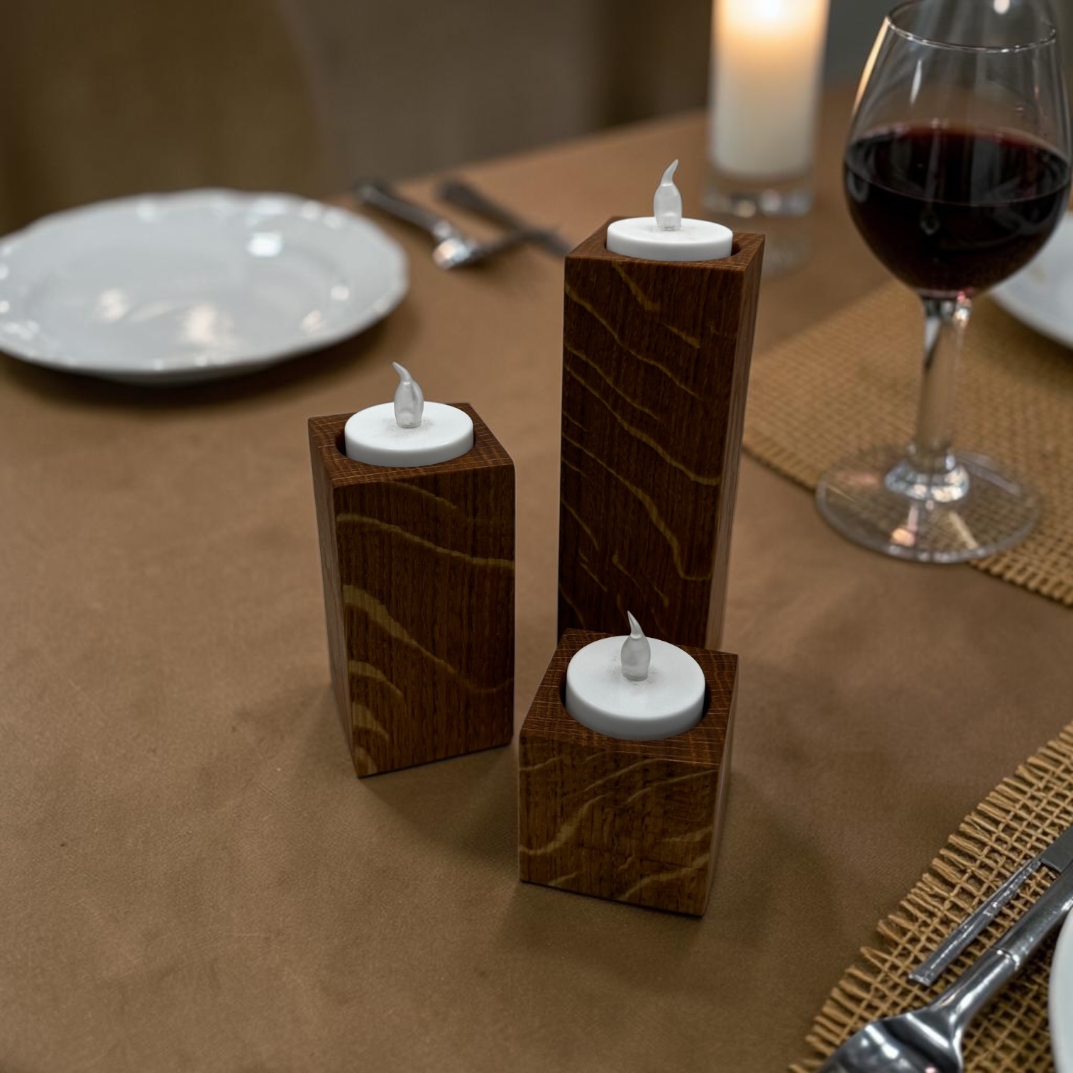 A trio of tea light holders, small, medium and large at a brown table with a glass of wine.