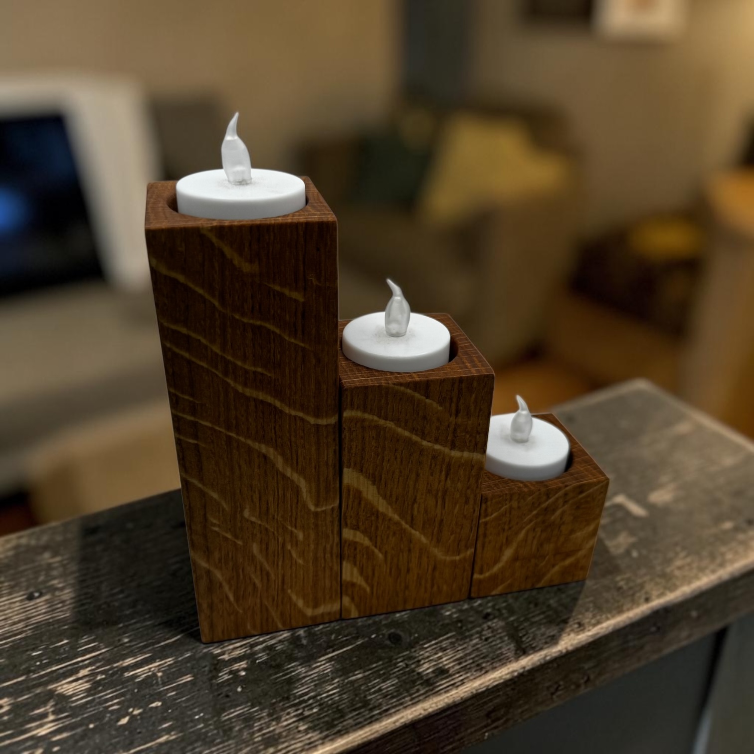 A stacked trio of tea light holders, small, medium and large on a wooden stair banister.