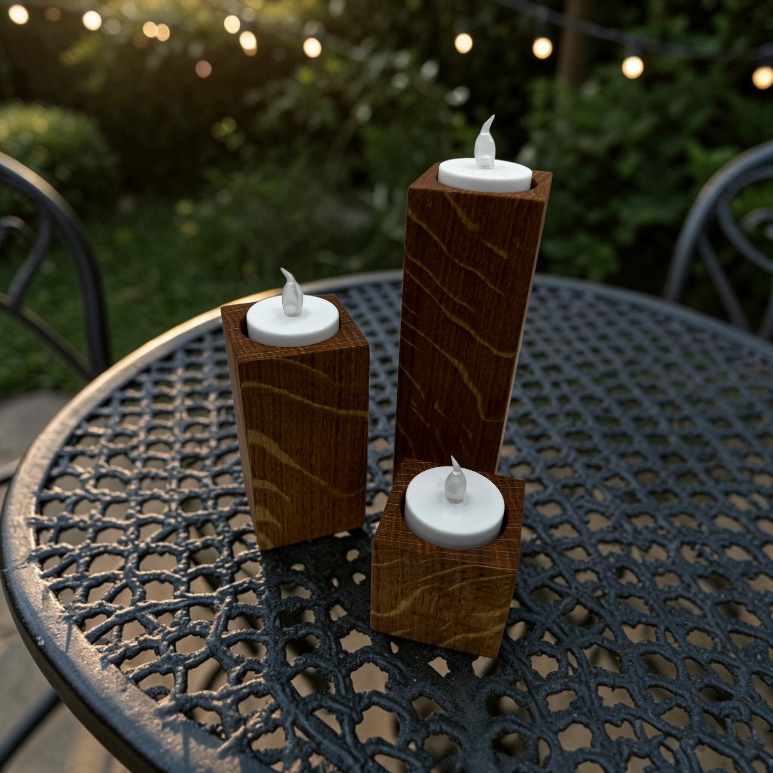A trio of tea light holders, small, medium and large at a bistro table outside with festoon light around the garden.