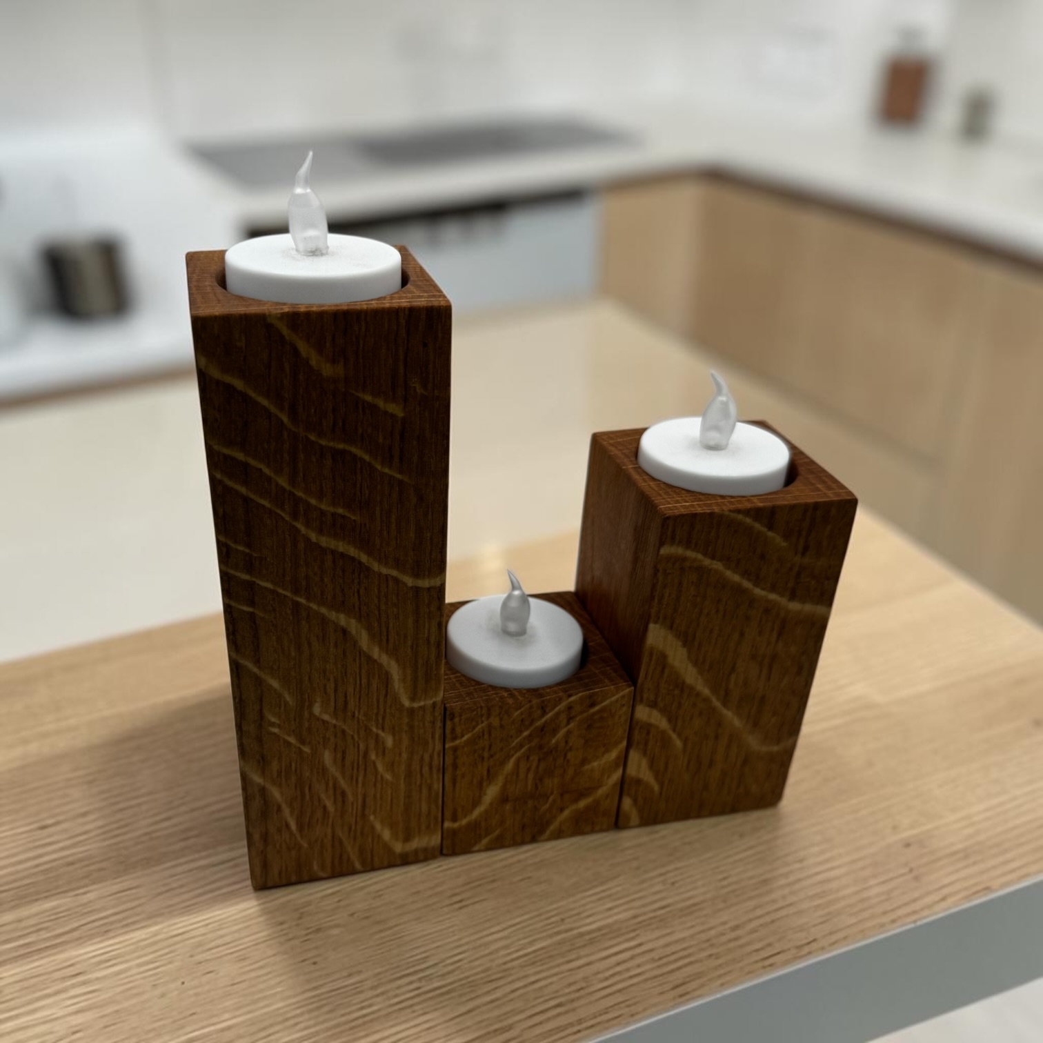 A stacked trio of tea light holders, small, medium and large at a modern oak kitchen island.